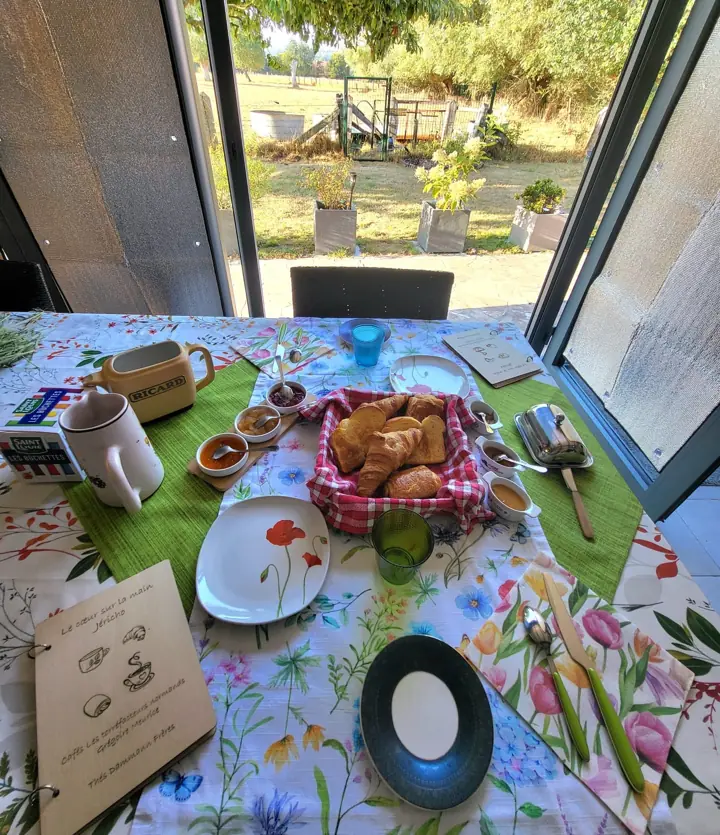 Une table dressée pour le petit-déjeuner, avec une grande fenêtre ouverte sur le jardin