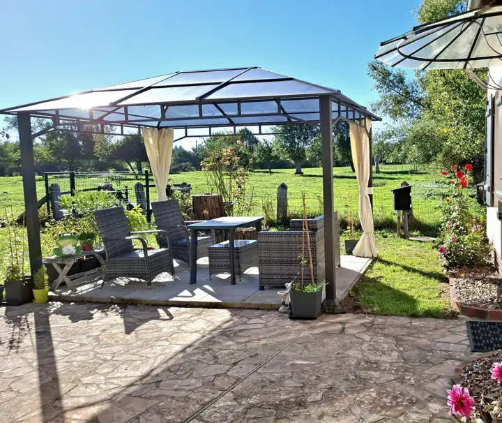 La tonnelle et son salon de jardin, face au pré, un jour de grand soleil